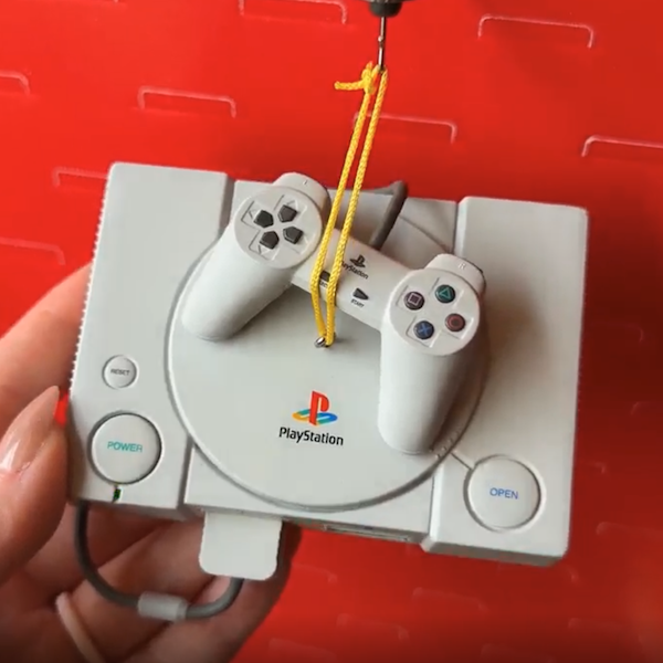 A woman's hand holds up a Keepsake Ornament that looks like the original PlayStation video game console from the 1990s.